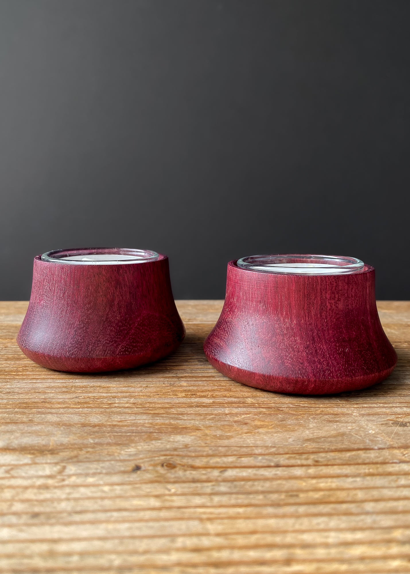 Two purpleheart wooden candle holders with glass inserts on wooden table