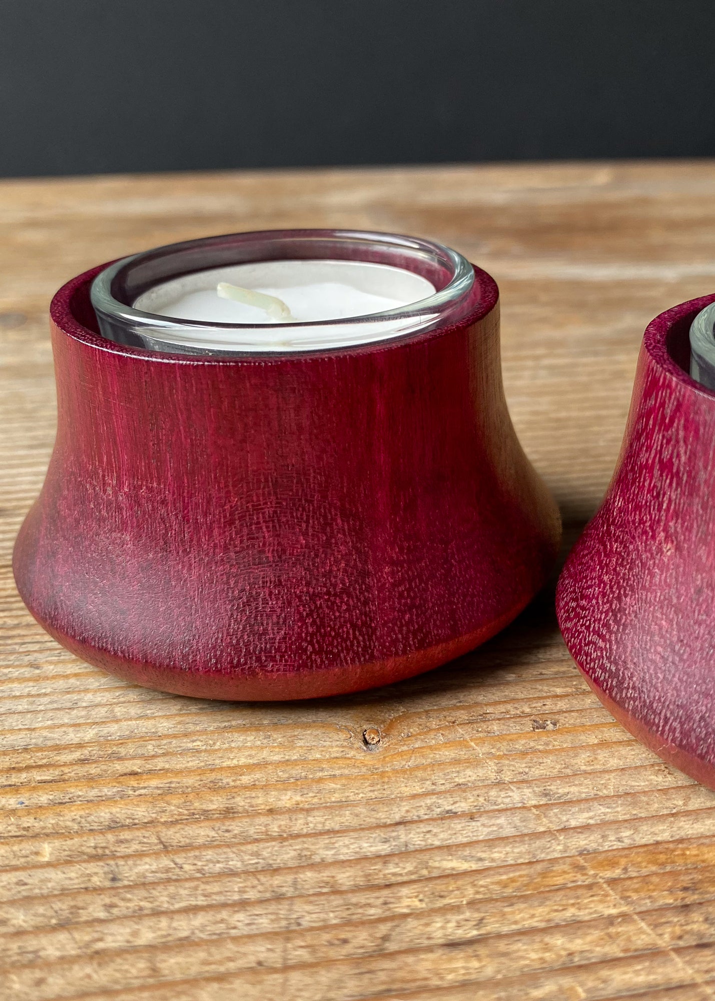 Close up of two Purpleheart wooden candle holders with glass inserts and tea light candles on wooden table.