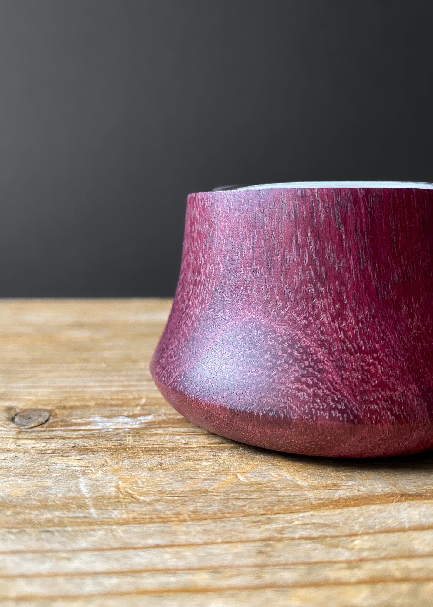 Close-up side view of Purpleheart wooden candle holder with glass insert on wood table.