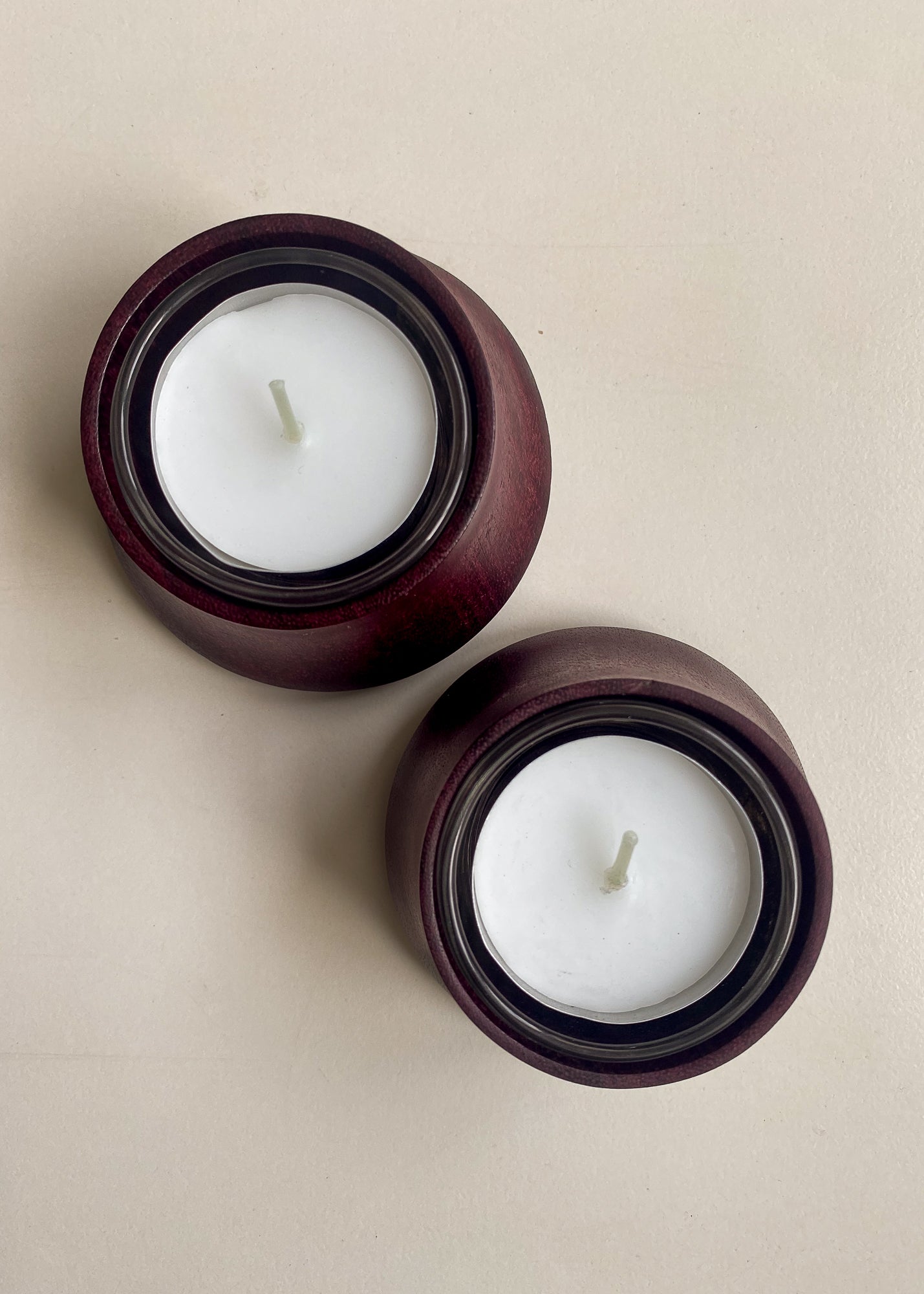 Overhead view of two Purpleheart wooden candle holders with glass inserts and tea light candles on white background.