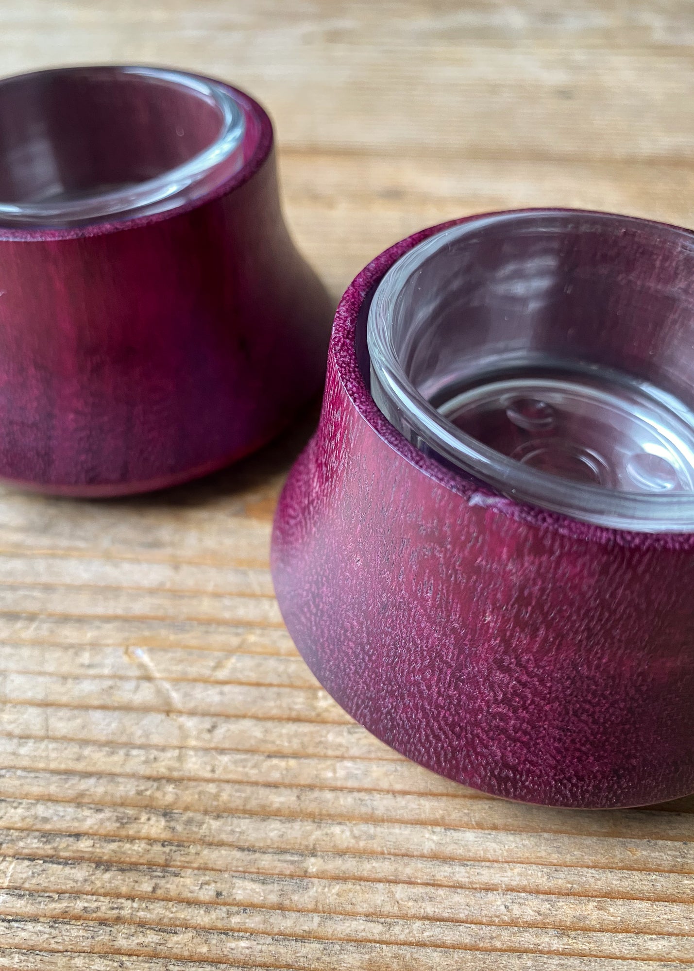 Close up view of two Purpleheart wooden candle holders with glass inserts on wooden table.