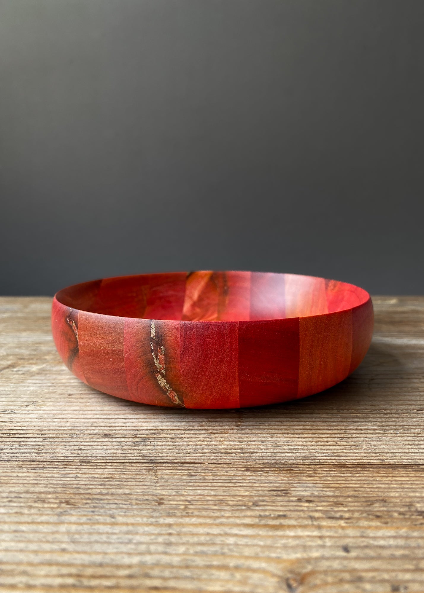 Segmented Pink Ivory wooden bowl with bronze detail on wood table.