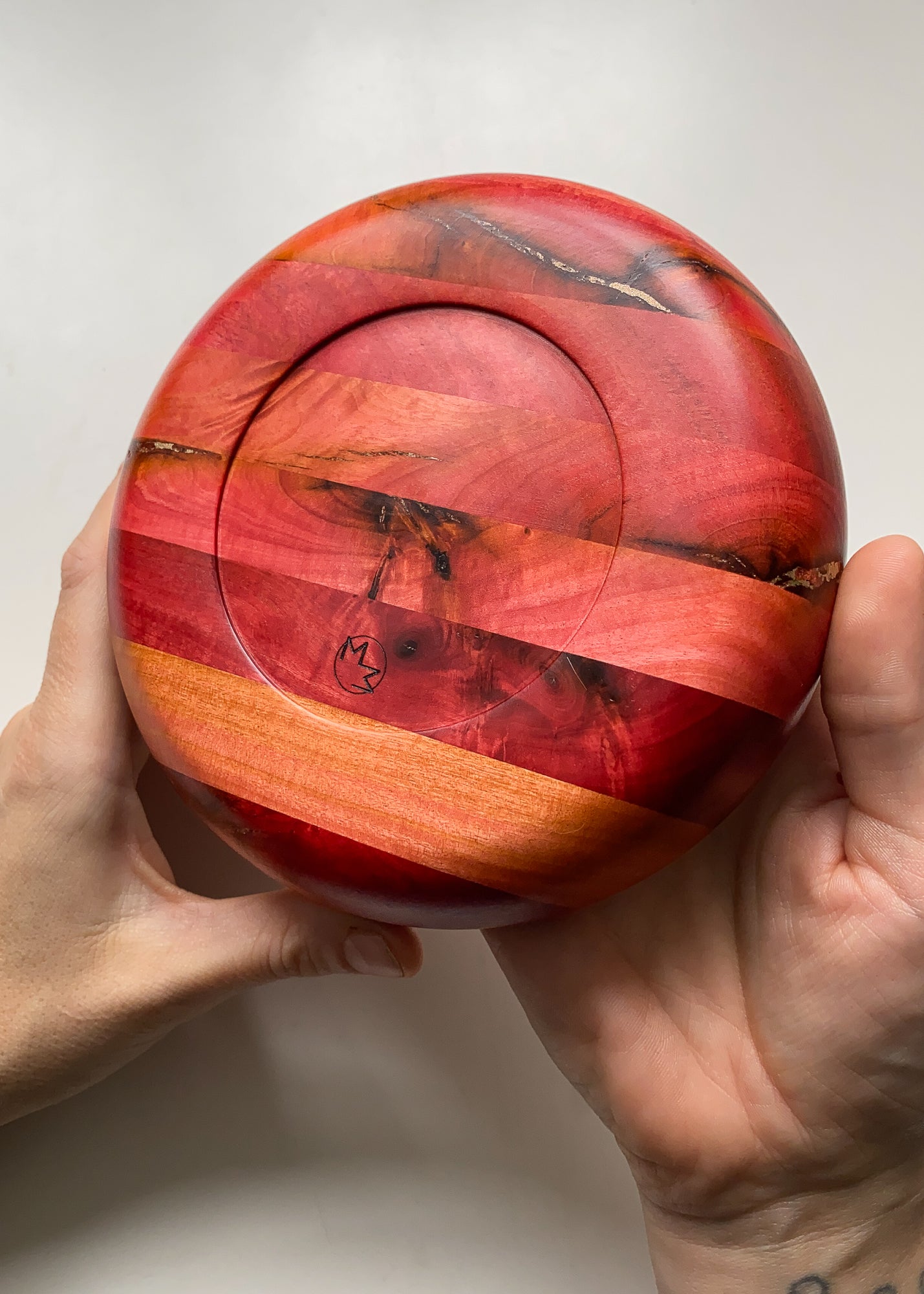 Underside view of Pink Ivory wooden bowl held in hands showing engraved logo on white background.