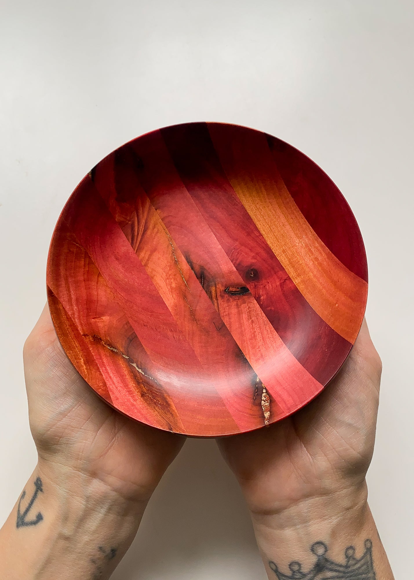 Overhead view of segmented Pink Ivory wooden bowl held in hands on white background.
