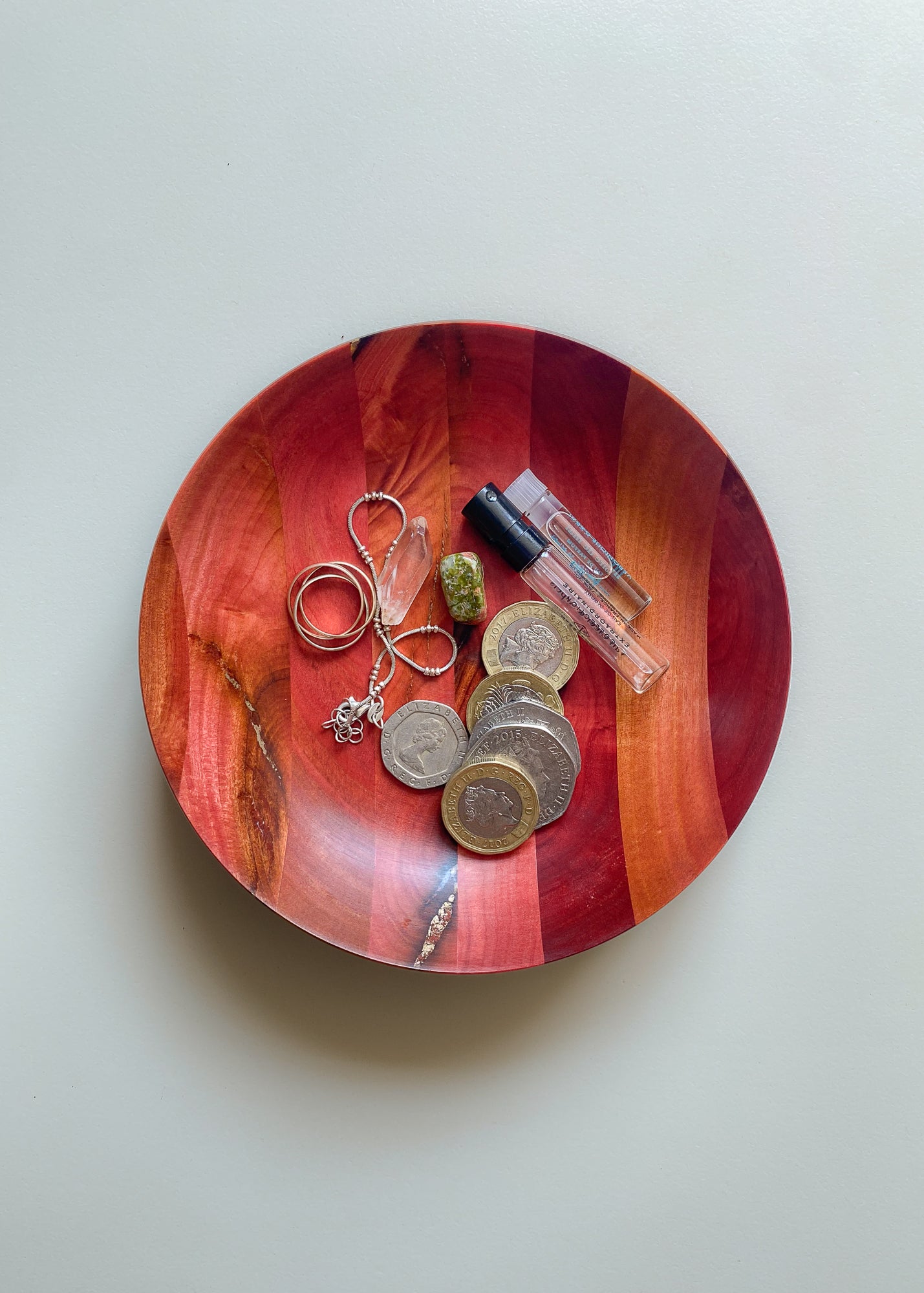 Overhead view of segmented pink and bronze wooden bowl with jewelry and trinkets on white background.