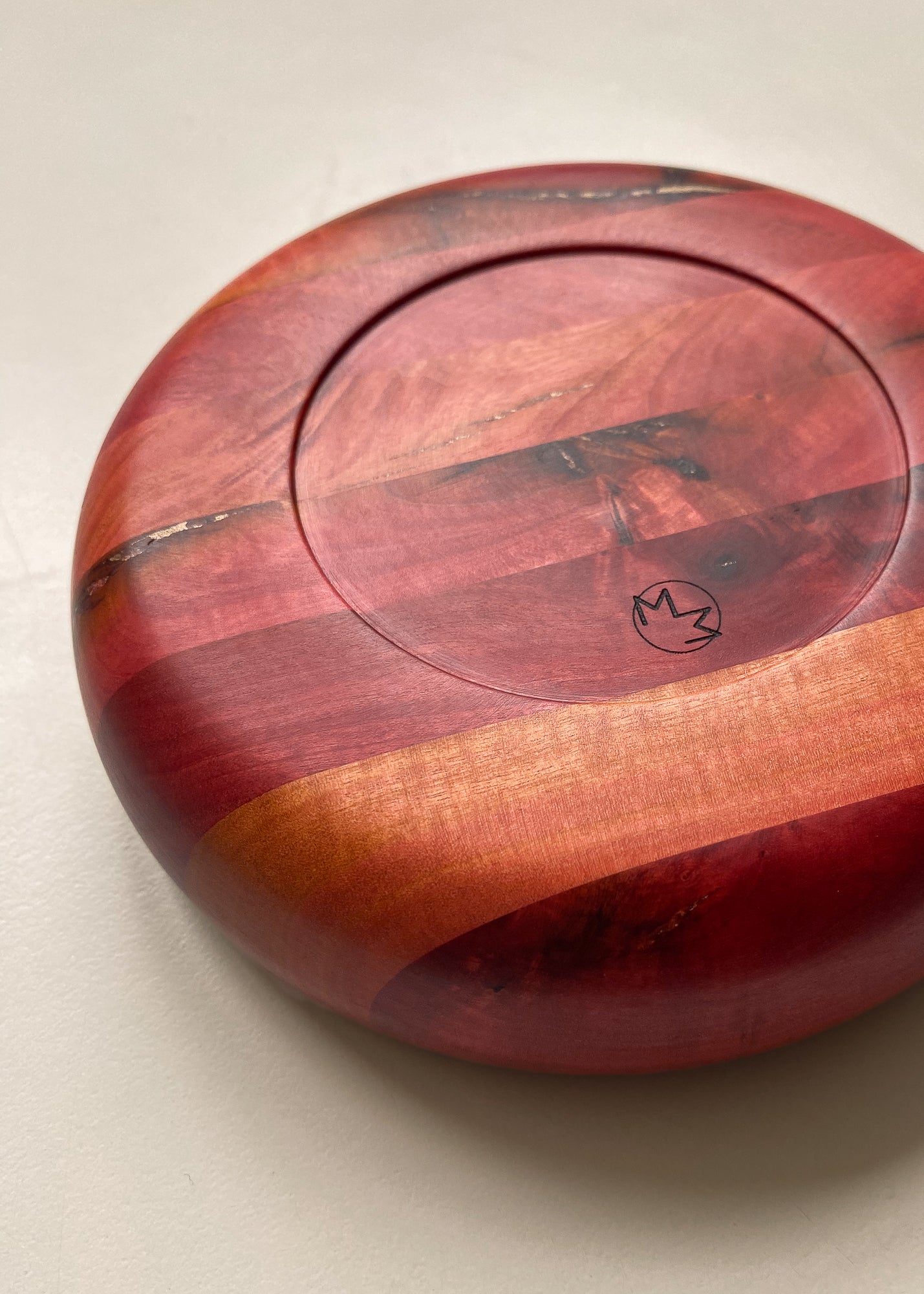 Underside view of segmented pink wooden bowl with engraved logo on white background.