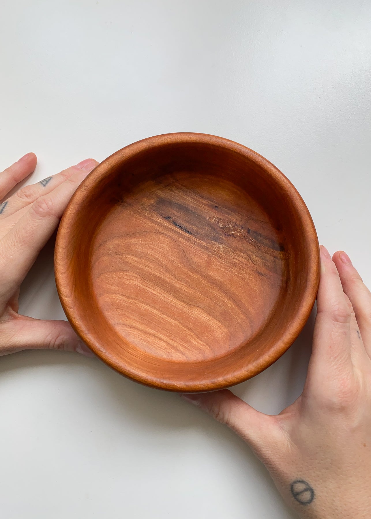 Overhead view of Cherry wood bowl held in hands on white background.