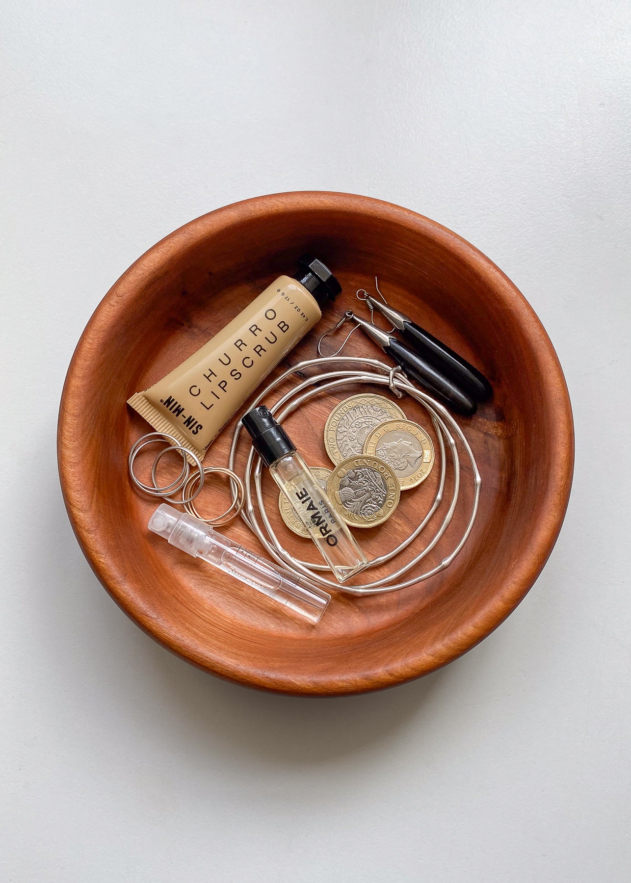 Overhead view of Cherry wood bowl with jewelry, perfume and lip balm on white background.