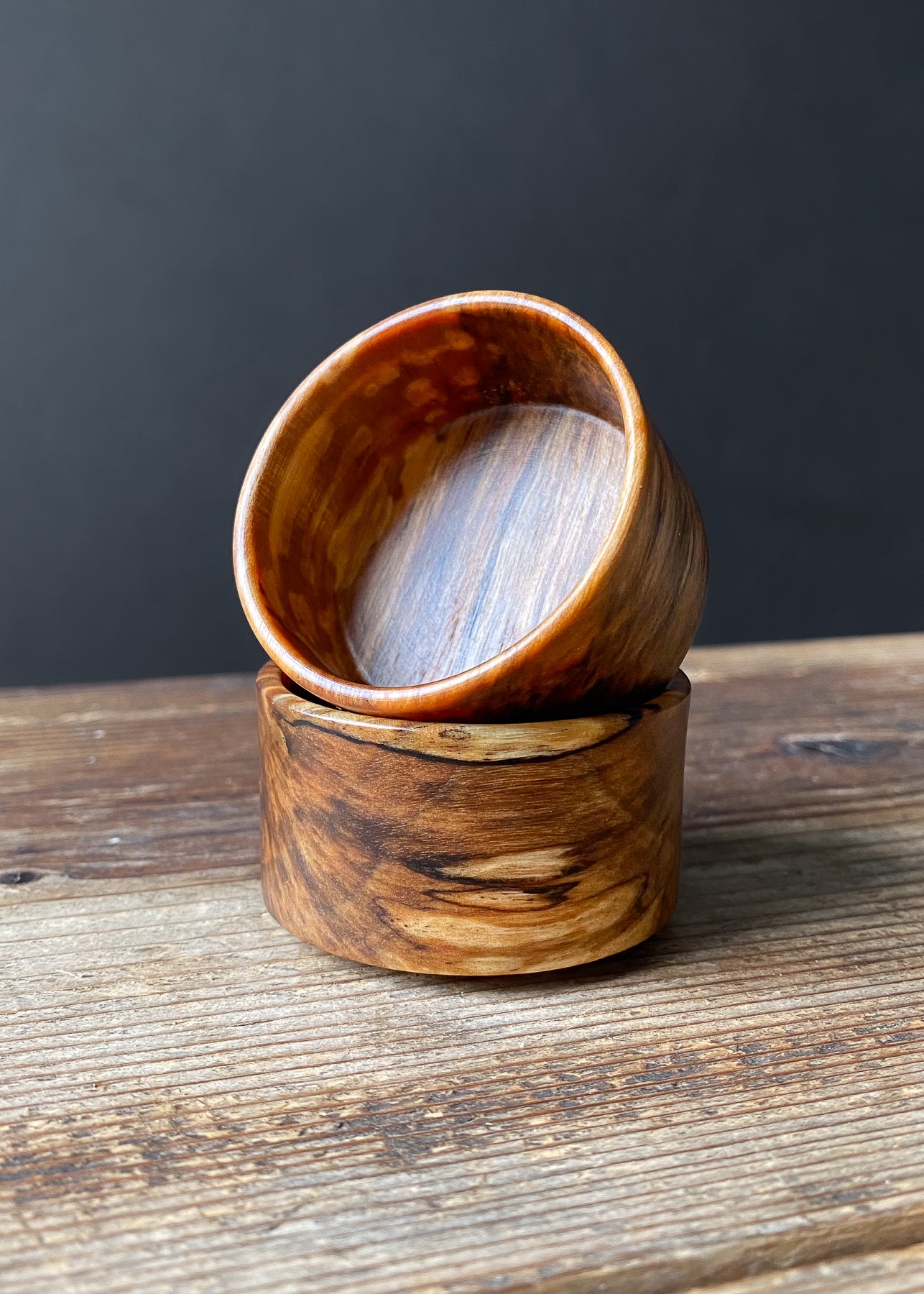 Two small spalted wooden bowls stacked on wood table.
