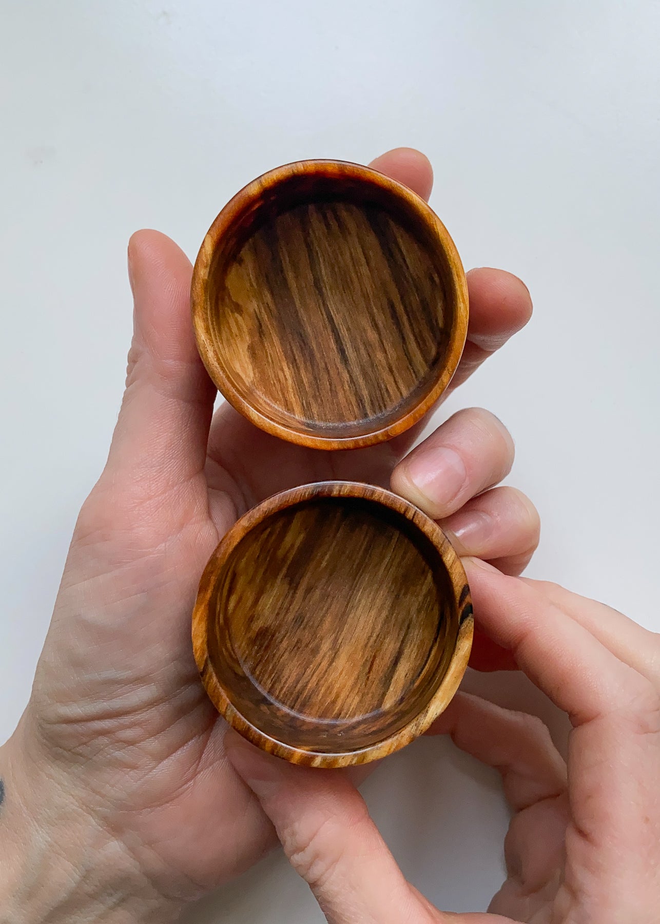 Overhead view of two small spalted wooden bowls held in hands on white background.