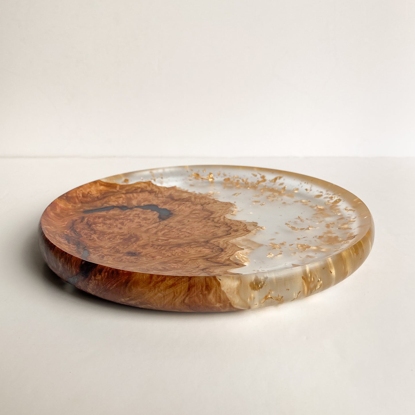 Round live-edge plate with resin and gold leaf against white background.