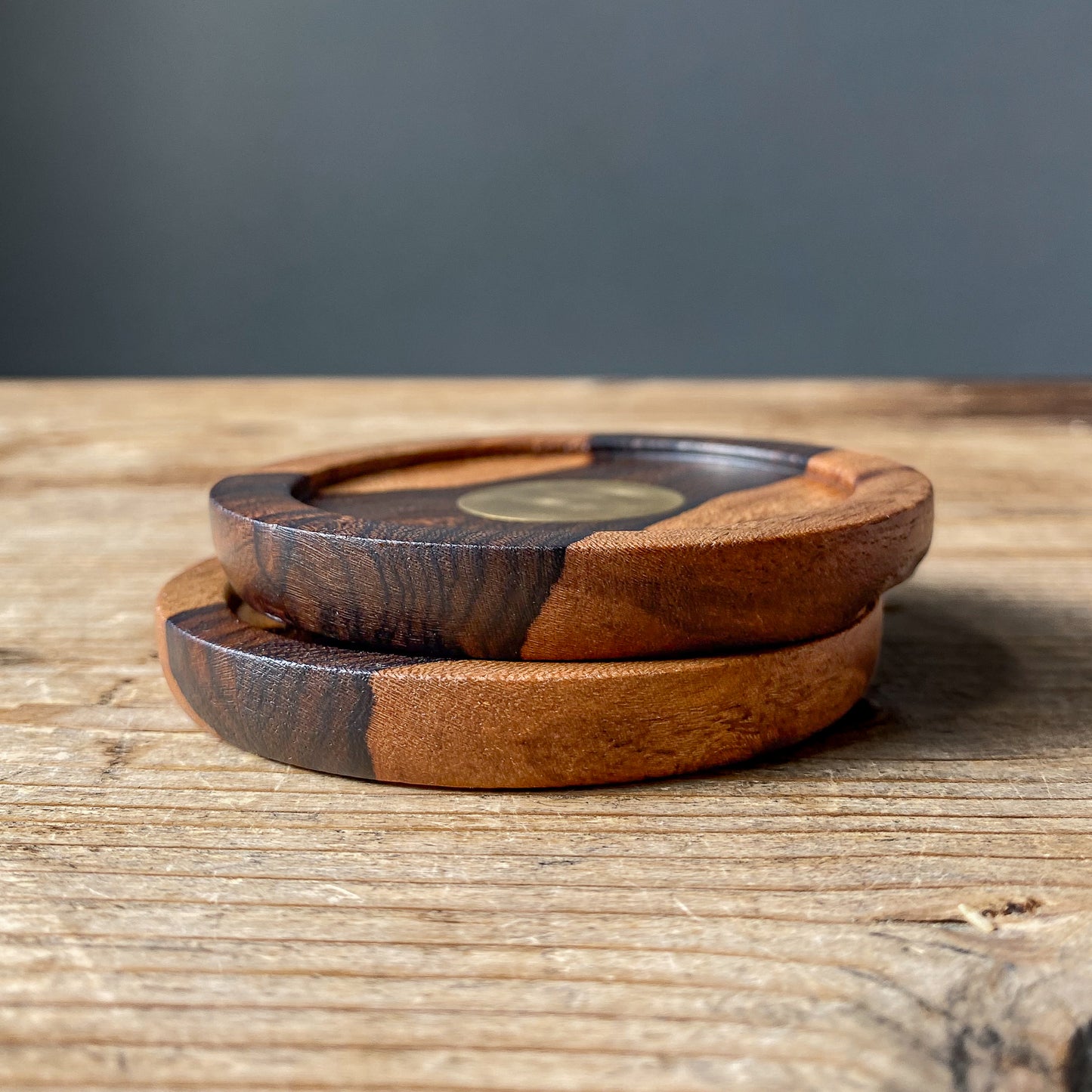 Close up view of two small Ziricote plates with brass detail on wooden table.