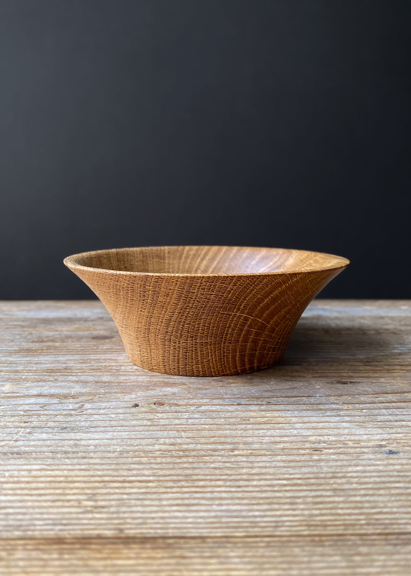 Oak wood bowl with flared rim on wooden bowl against dark background.