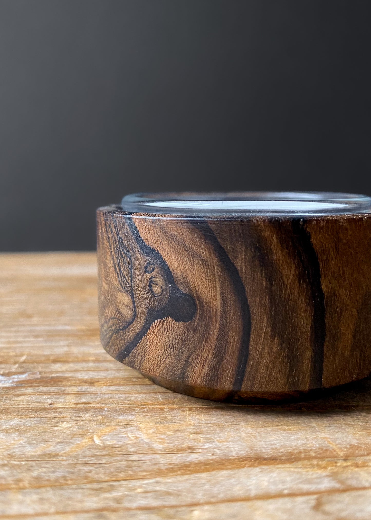 Close up side profile of Ziricote wood candle holder with glass cup on wooden table.