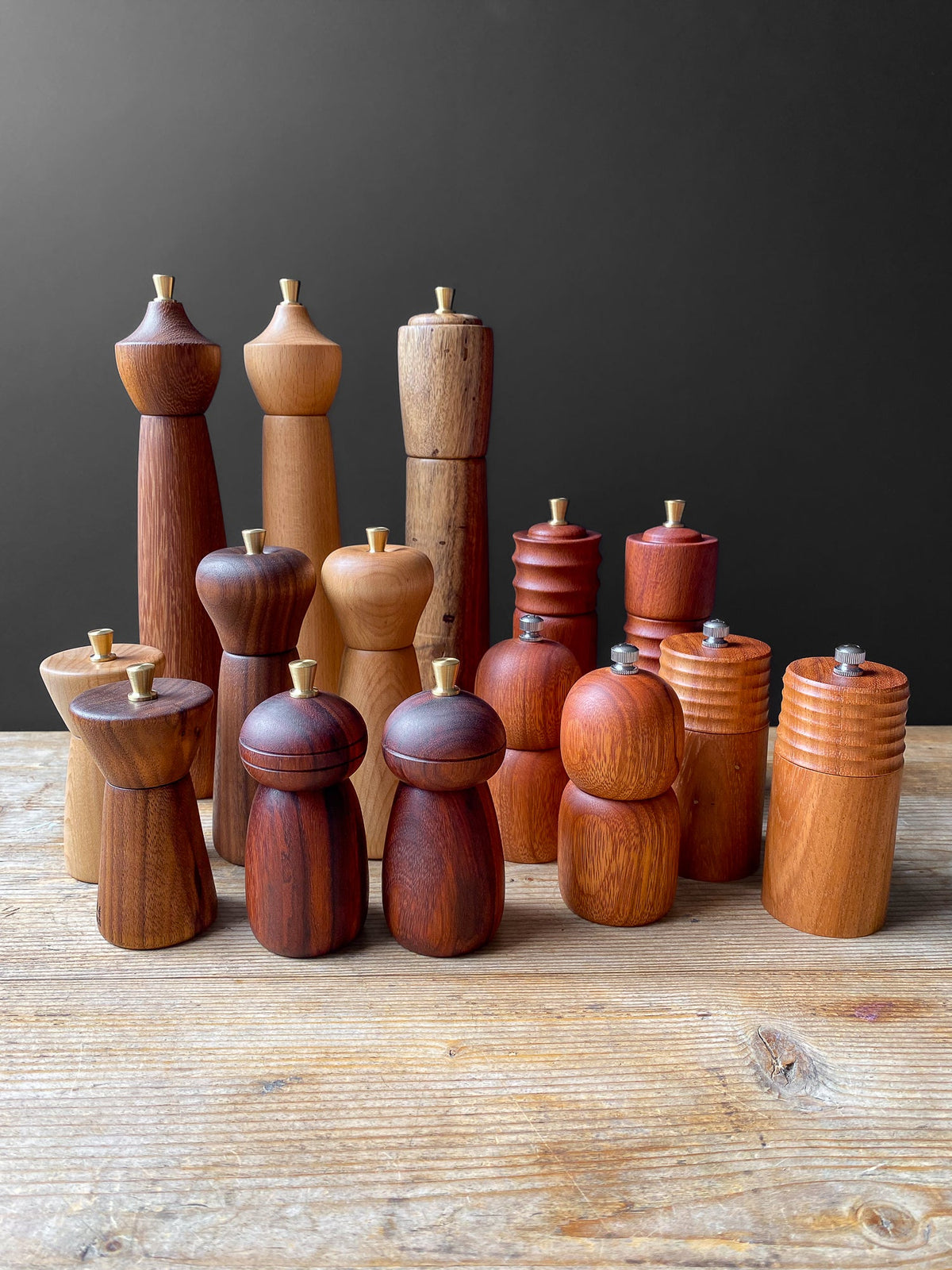 Collection of wooden pepper mills on a wooden surface with a dark background