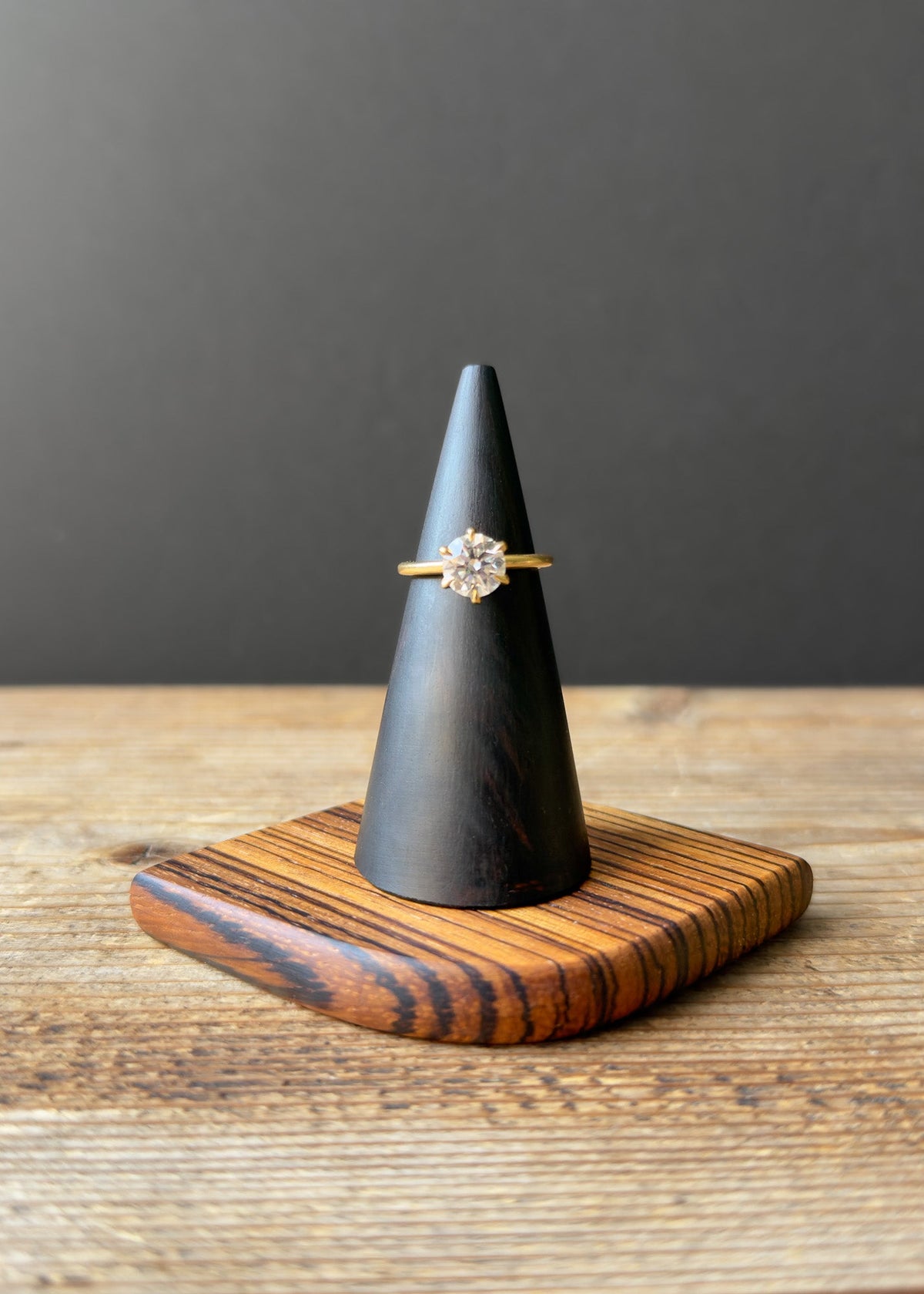 Ring on a black wooden cone-shaped stand with a striped wooden base against a dark background