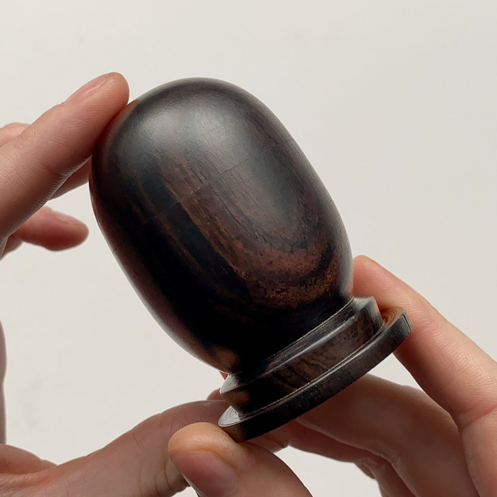 Small African Blackwood lidded box held in hands against white background.