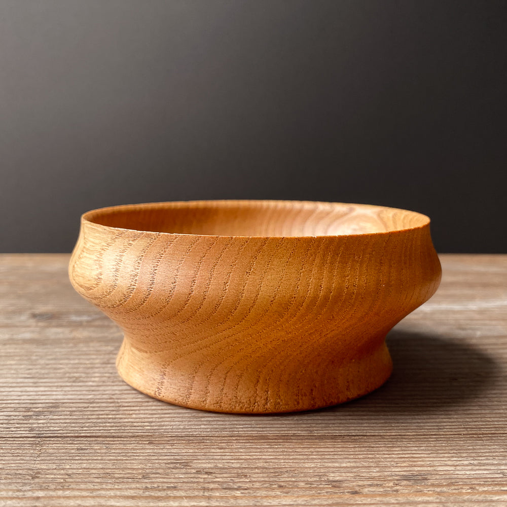 Wooden bowl with curved shape on a wooden surface with a dark gray background