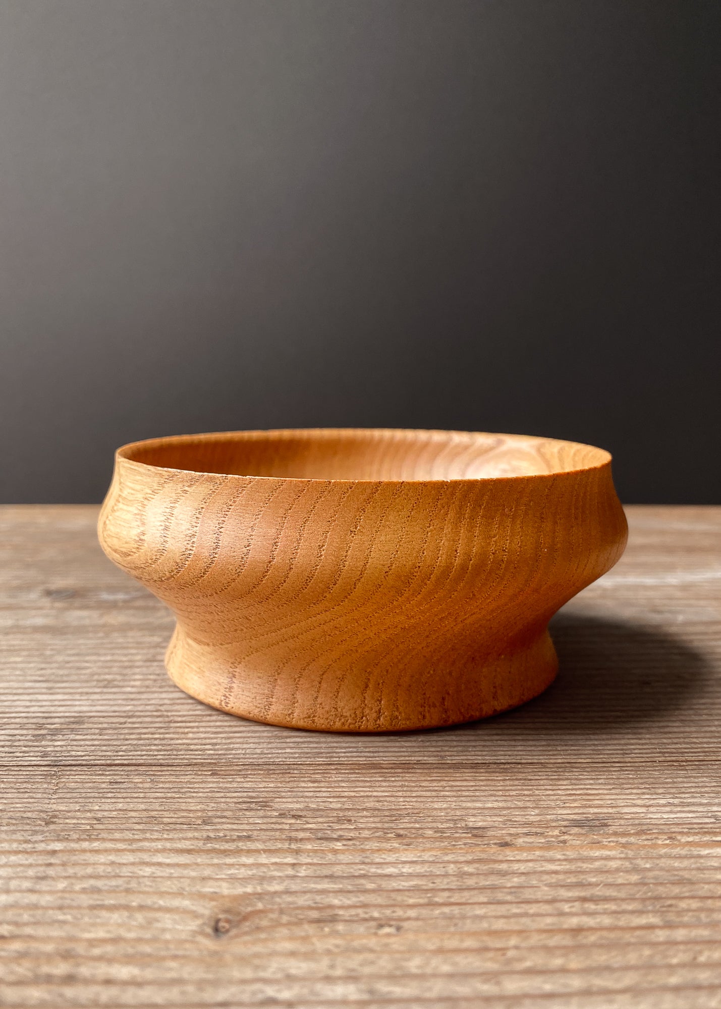 Wooden bowl with curved shape on a wooden surface with a dark gray background