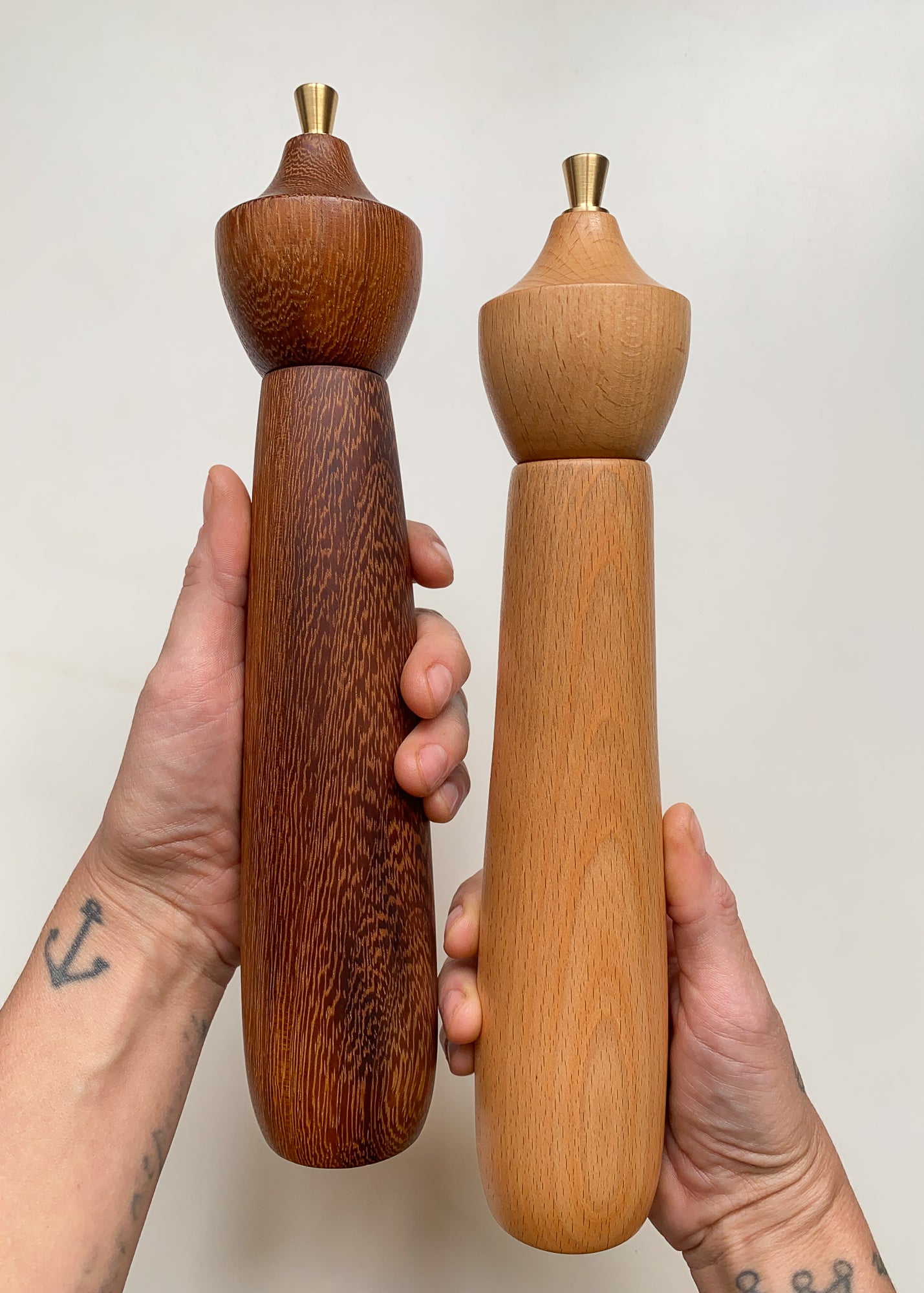 Two wooden pepper mills held in hands against a plain background