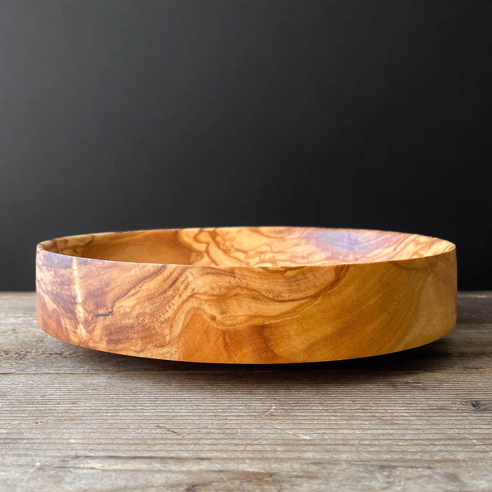 Patterned olive wood bowl on wooden table.