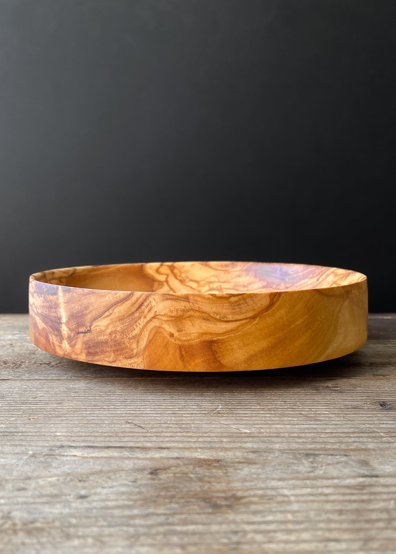 Patterned olive wood bowl on wooden table.