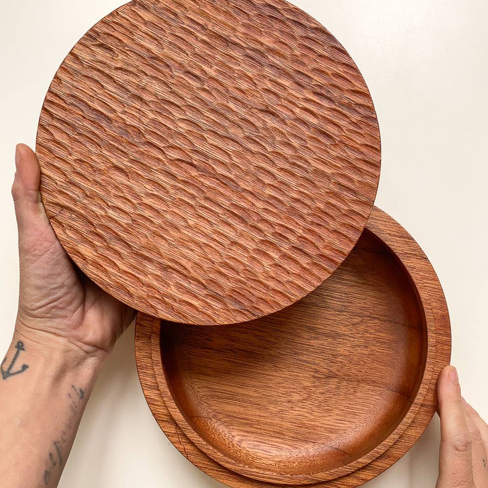 Overhead view of large wooden box with textured lid held open in hands against white background.