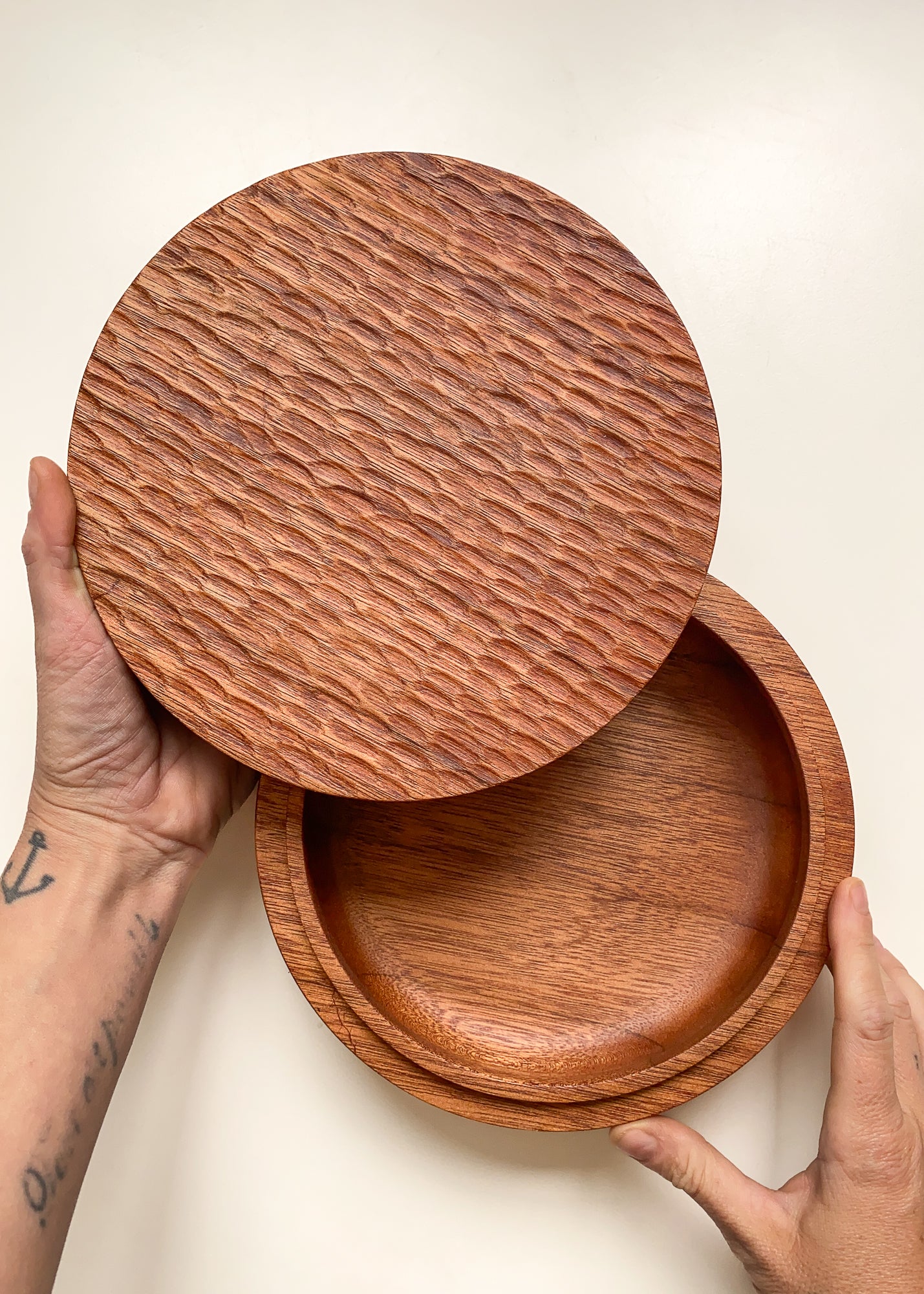 Overhead view of large wooden box with textured lid held open in hands against white background.
