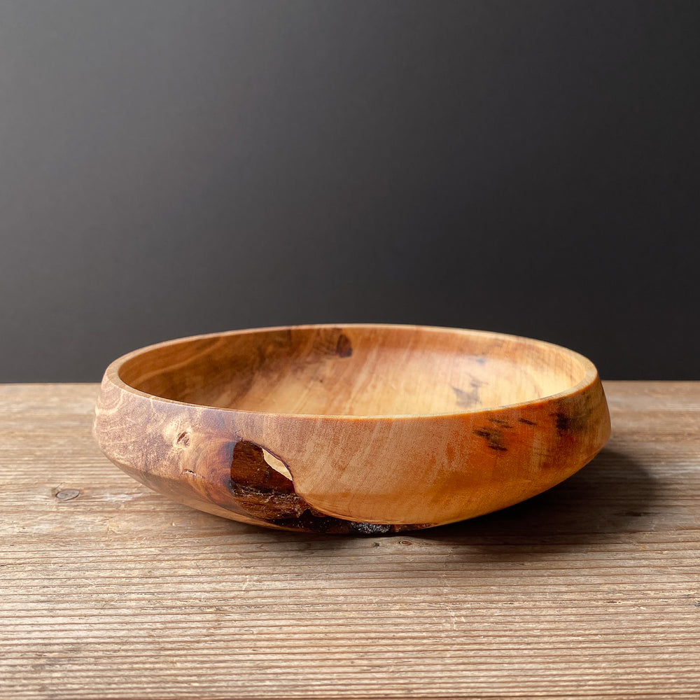 Live edge Tulip wood bowl on wooden surface with black background.