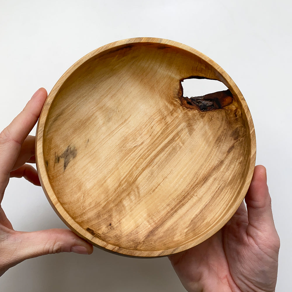 Live edge tulip wood bowl held by hands against a white background