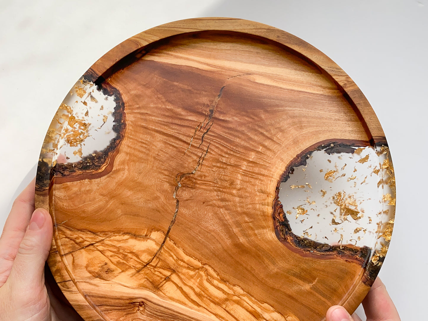 Olive wood, resin and gold leaf tray with natural edge design held by a hand on a white background.
