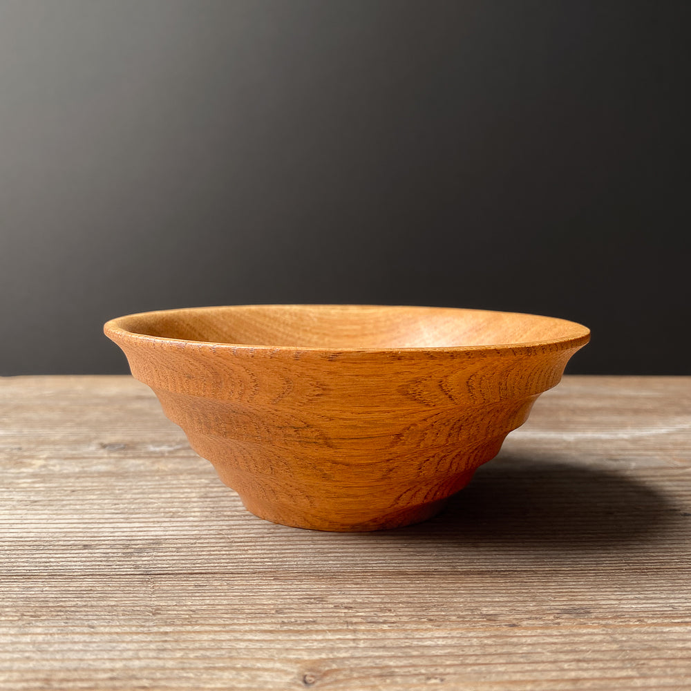 Light brown Chestnut Oak wood bowl with ribbed shape on wooden table.