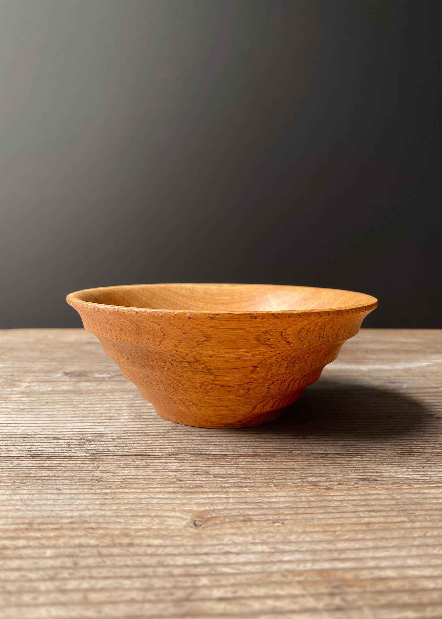Light brown Chestnut Oak wood bowl with ribbed shape on wooden table.