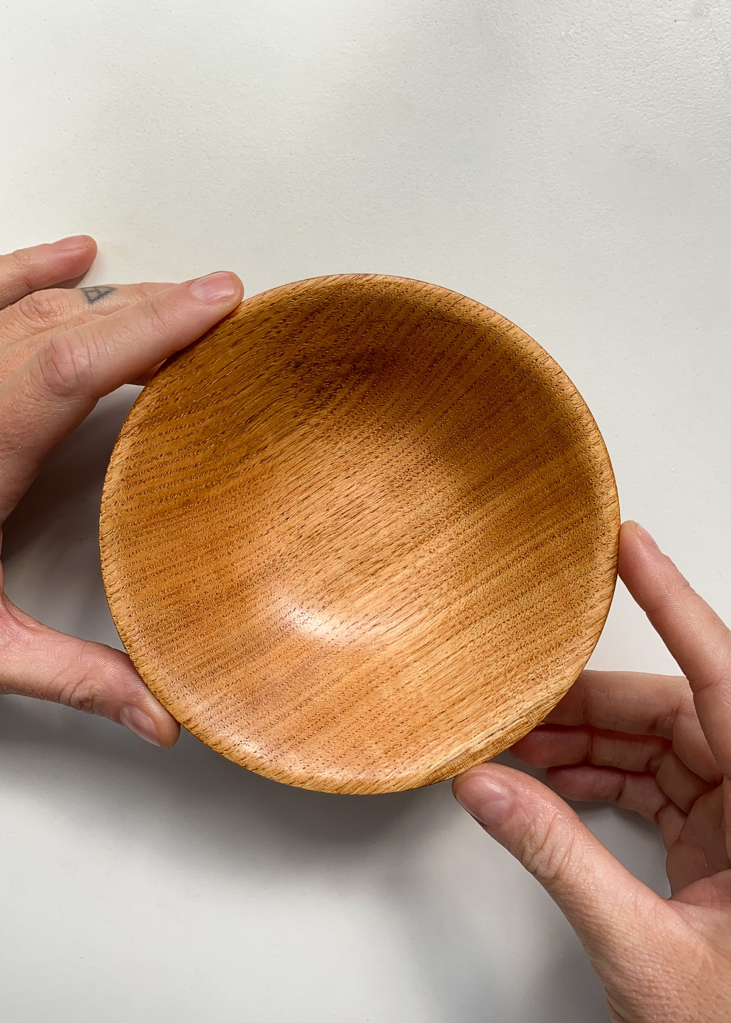 Overhead view of wooden bowl held by two hands against a plain background