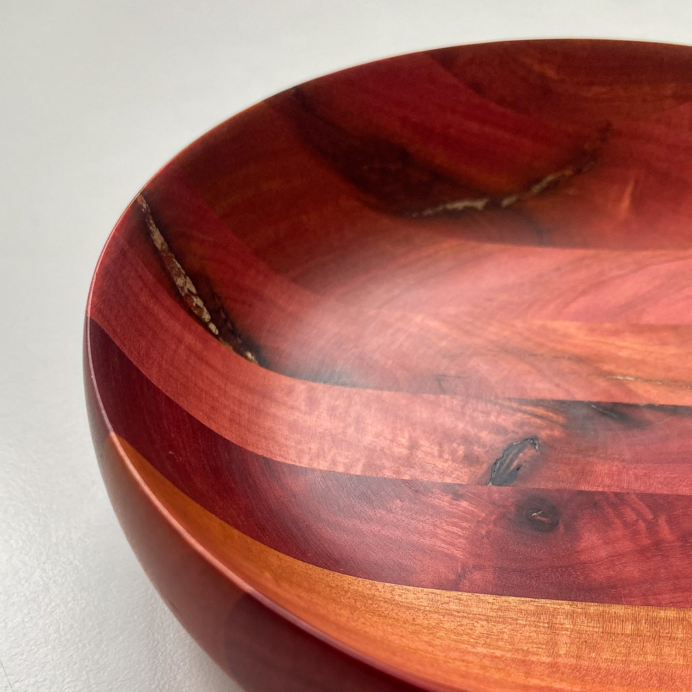 Close up of segmented Pink Ivory wooden bowl with bronze inlay against white background.