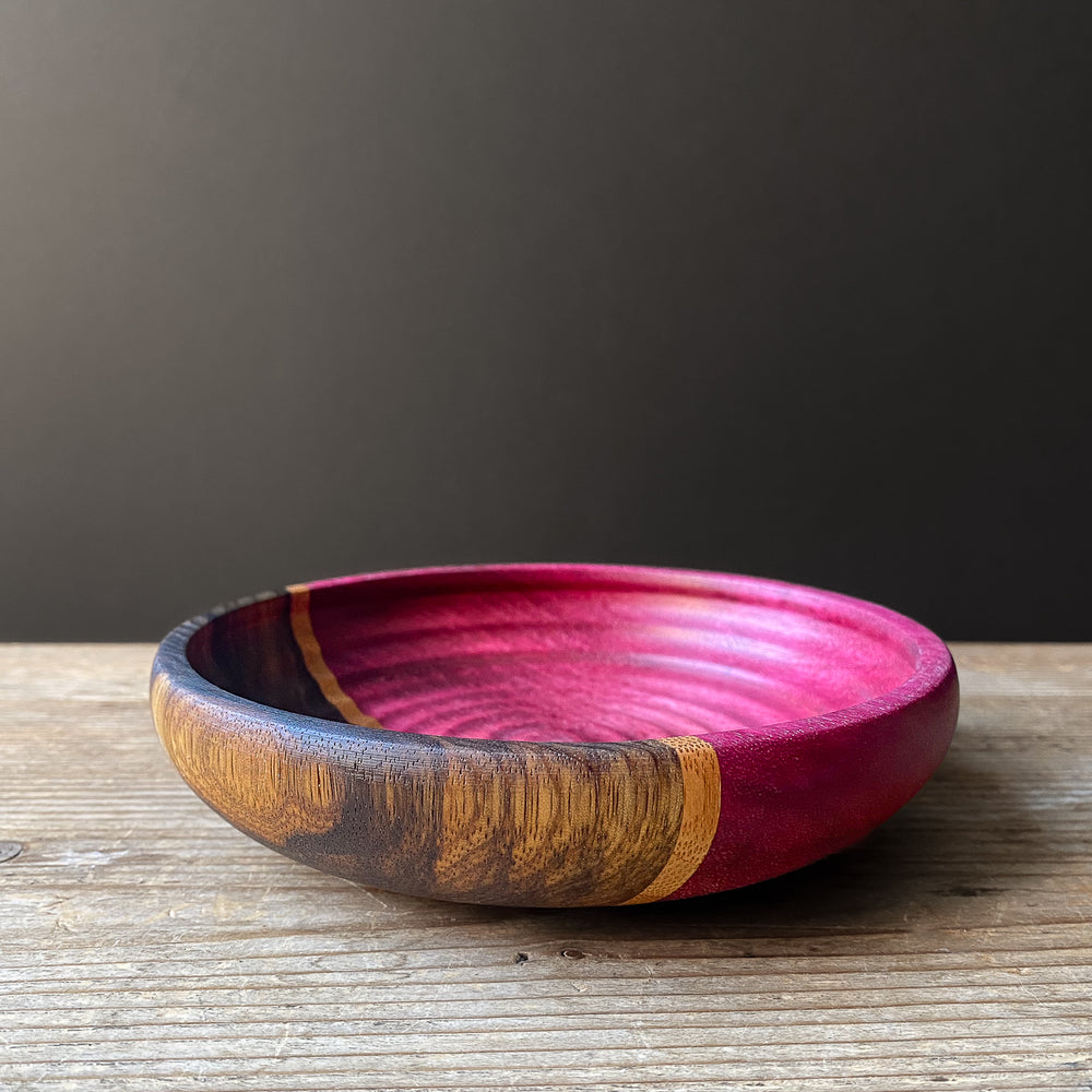 Purple and black segmented wooden bowl with rippled interior against minimalist background.