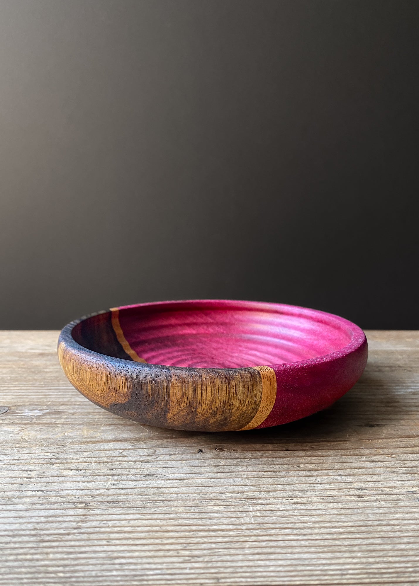 Purple and black segmented wooden bowl with rippled interior against minimalist background.