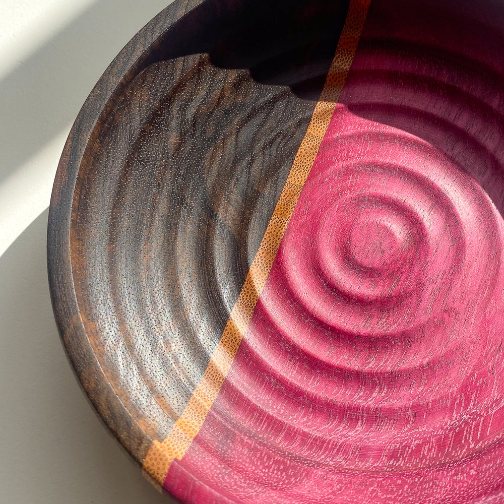 Close up view of segmented purple and brown wooden bowl with rippled texture in natural light on white background.
