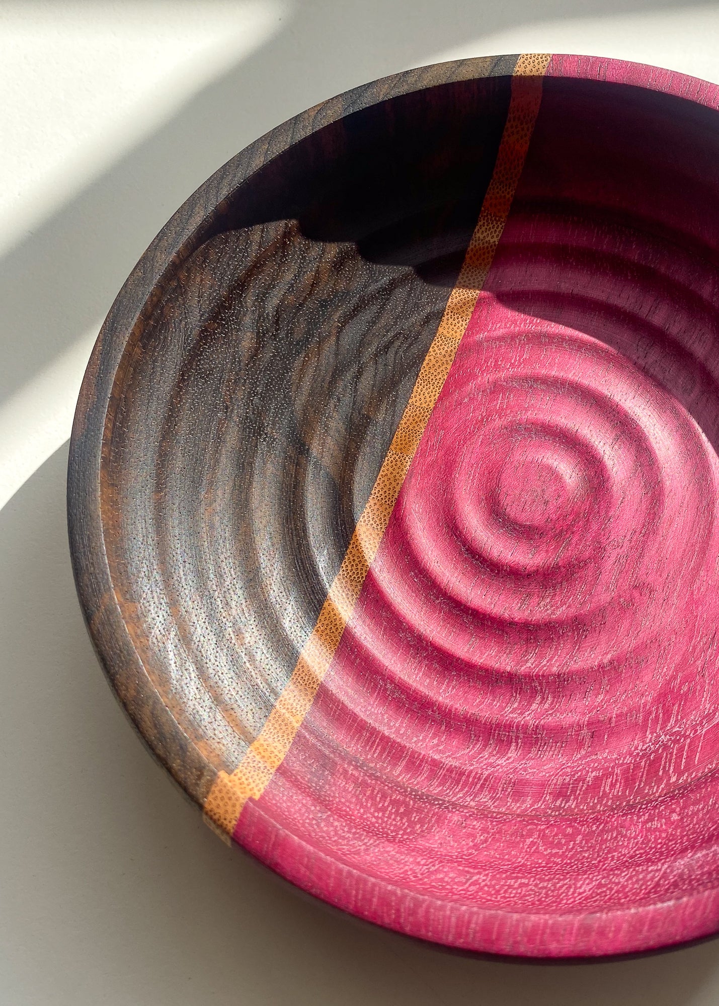 Close up view of segmented purple and brown wooden bowl with rippled texture in natural light on white background.