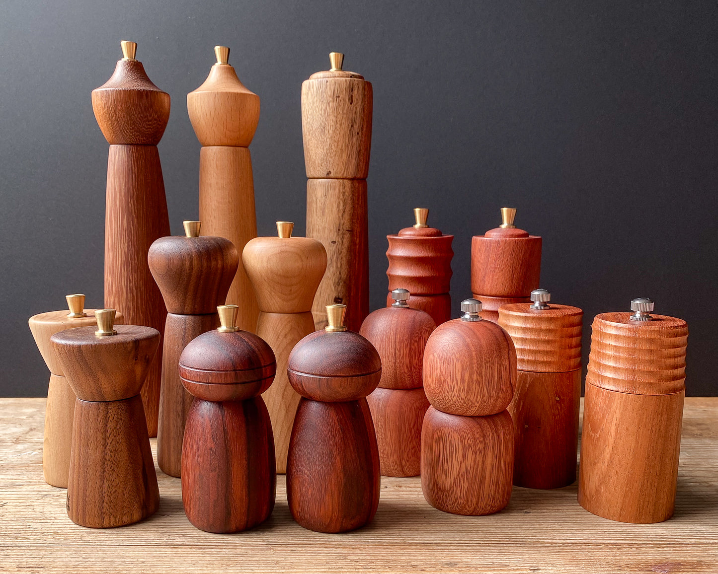 Collection of wooden pepper mills on a wooden surface with a dark gray background.