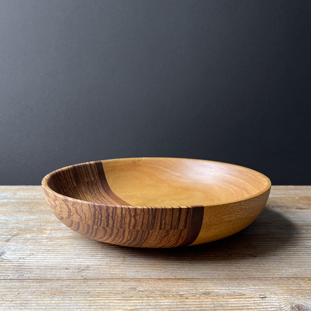 Orange and brown wooden bowl on wood table against dark background.