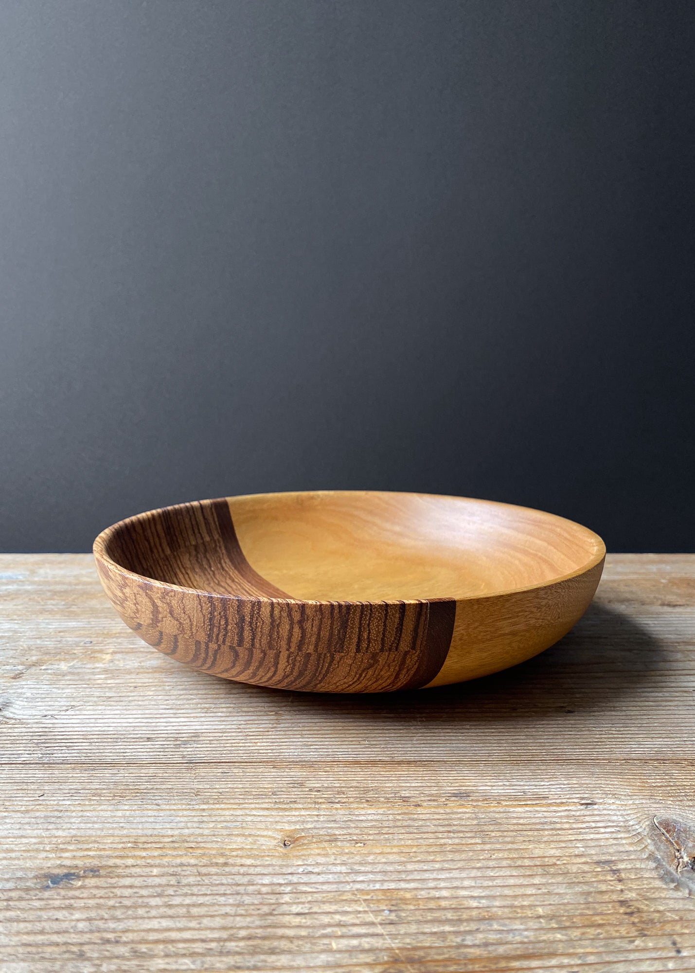 Orange and brown wooden bowl on wood table against dark background.