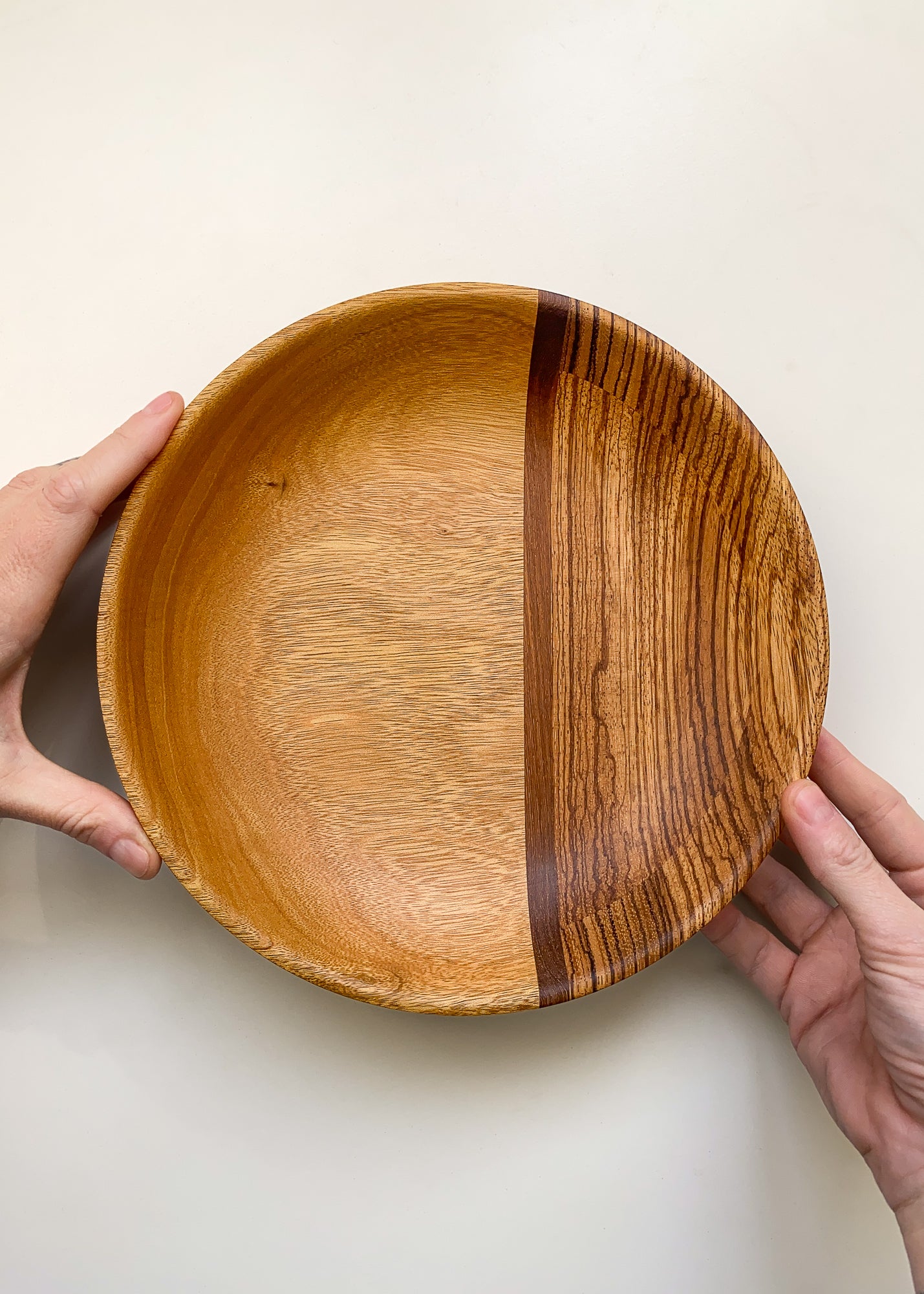 Segmented wooden bowl held in hands on a light background.