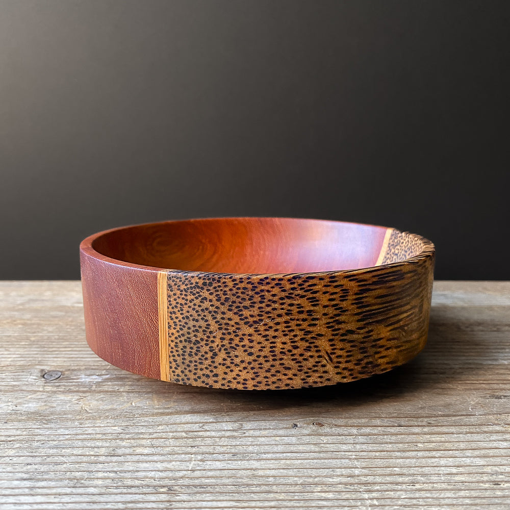 Segmented wooden bowl with speckled grain on wood table against dark background.