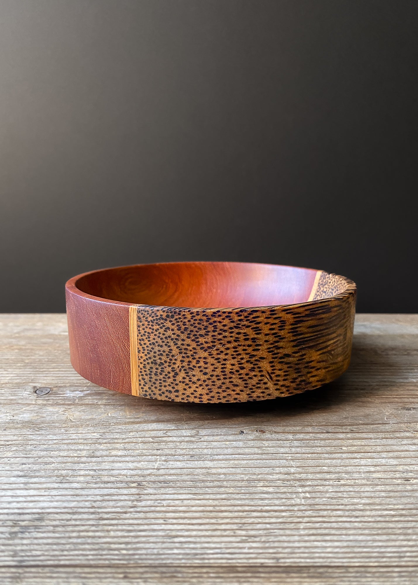Segmented wooden bowl with speckled grain on wood table against dark background.