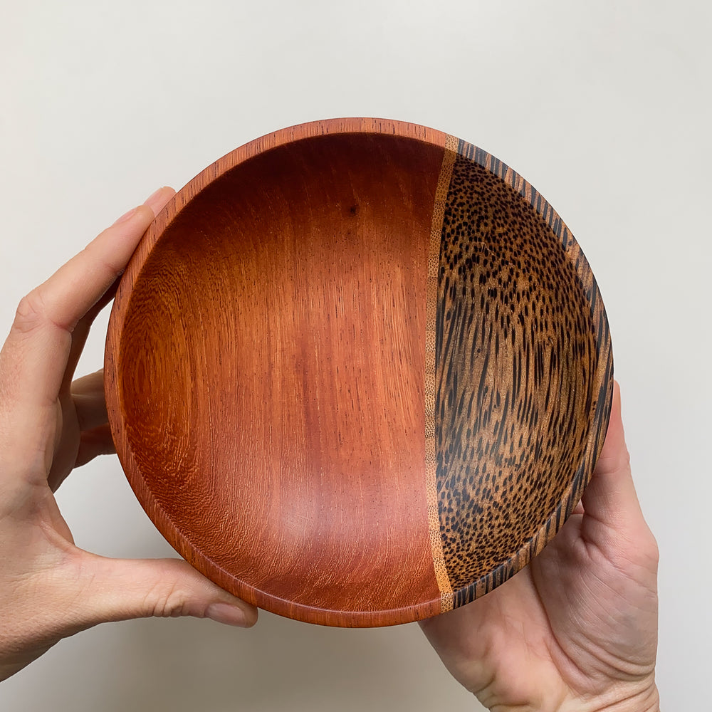 Segmented wooden bowl with reddish brown and speckled finish held in hands against light background.