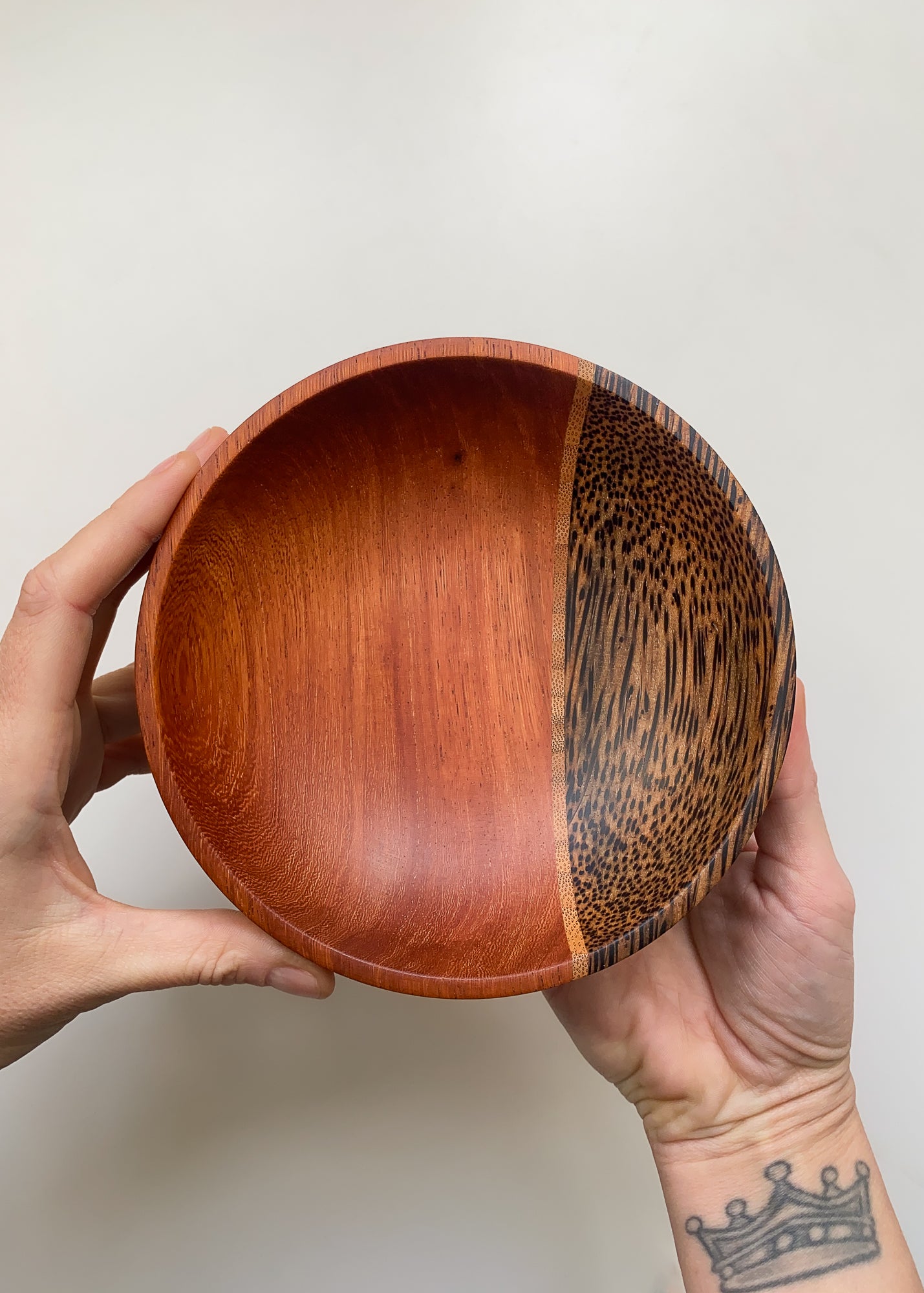 Segmented wooden bowl with reddish brown and speckled finish held in hands against light background.