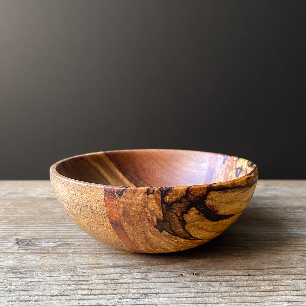 Rounded segmented wooden bowl on wood table against dark background.
