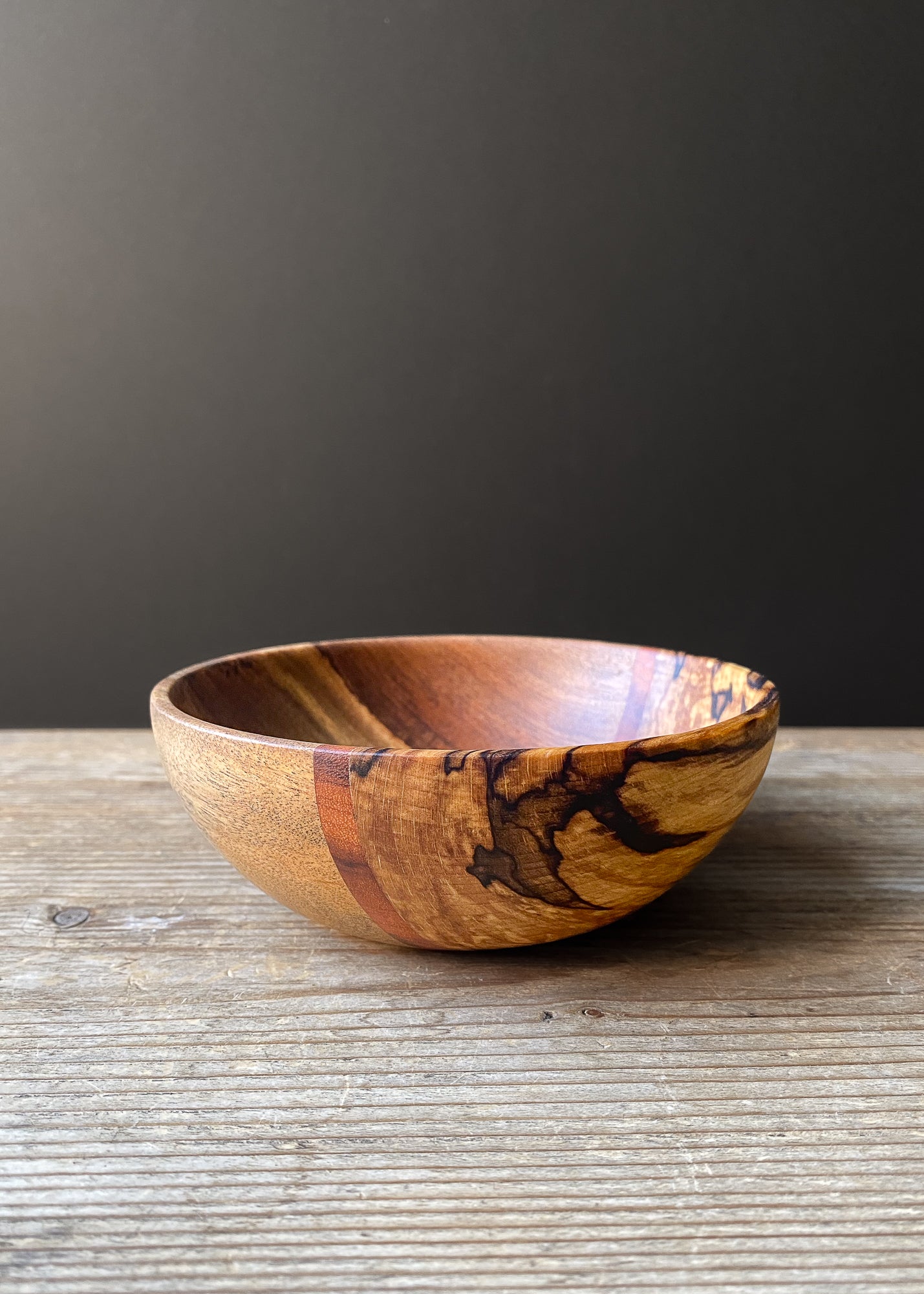 Rounded segmented wooden bowl on wood table against dark background.