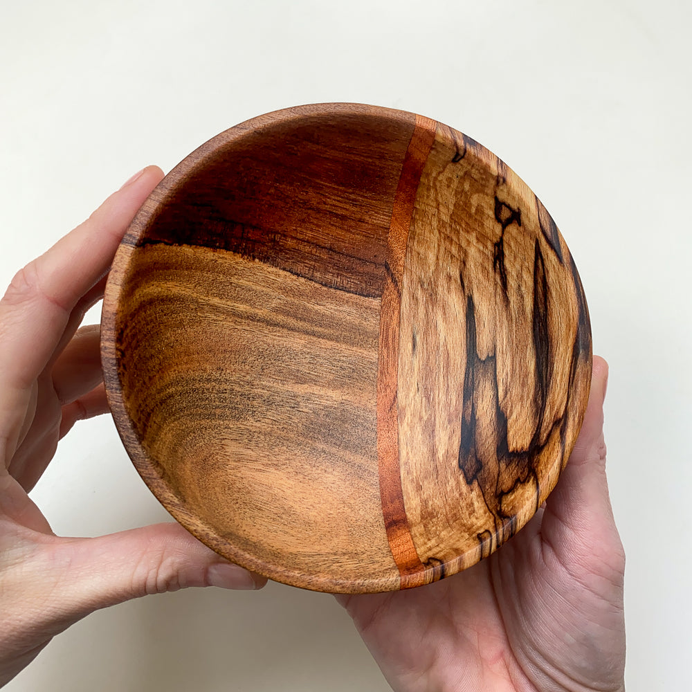 Small segmented wooden bowl held by a hand against a white background